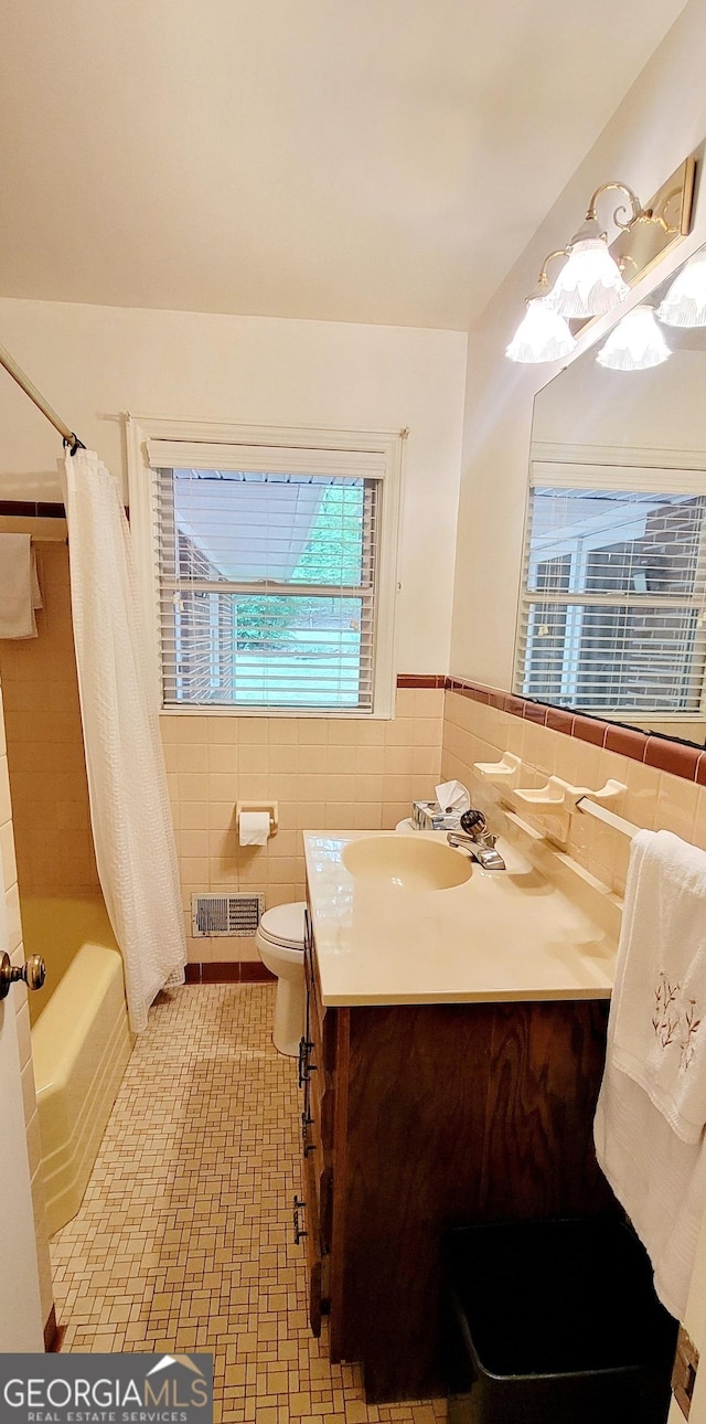 full bathroom with shower / bath combo, vanity, tile walls, toilet, and visible vents
