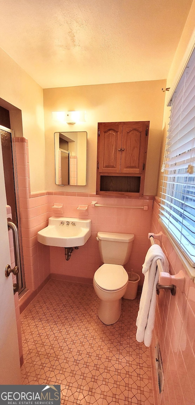 full bath featuring wainscoting, toilet, a sink, and tile walls
