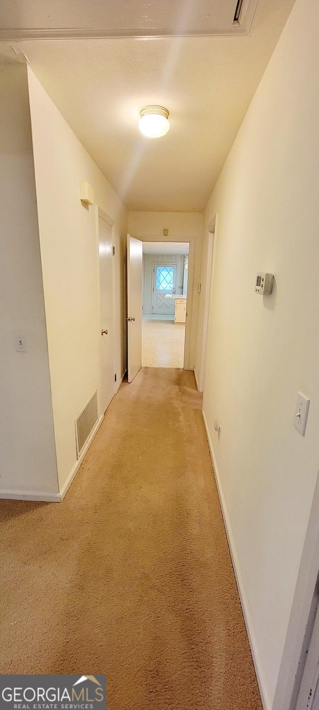 corridor with baseboards, visible vents, and light colored carpet
