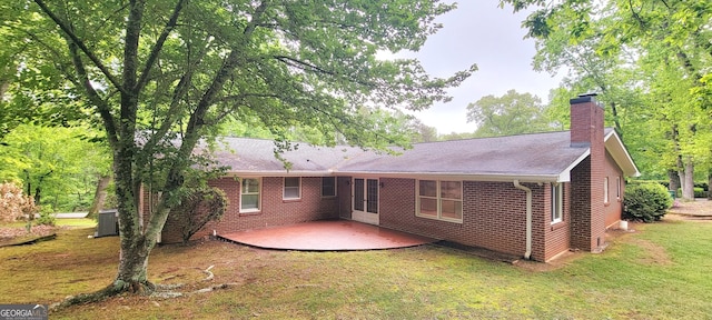 back of property featuring a chimney, central air condition unit, a lawn, brick siding, and a deck