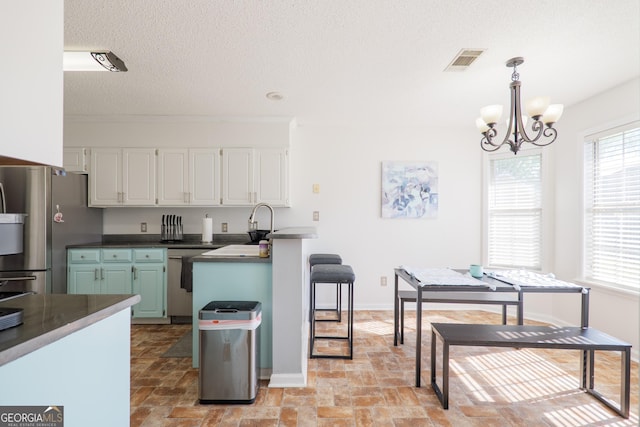 kitchen with an inviting chandelier, stainless steel appliances, white cabinetry, visible vents, and a kitchen breakfast bar