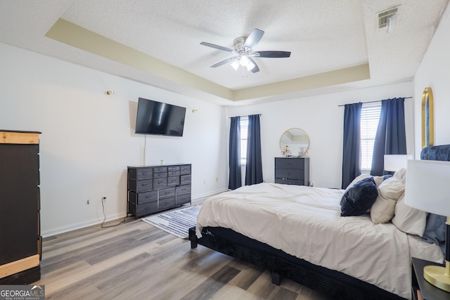 bedroom with a tray ceiling, visible vents, baseboards, a textured ceiling, and wood finished floors