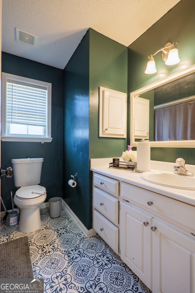 bathroom with a textured ceiling, visible vents, baseboards, toilet, and vanity