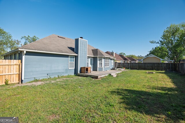 rear view of house with a chimney, a fenced backyard, a deck, and a lawn