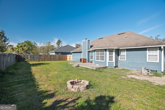 back of property with a lawn, a wooden deck, a fenced backyard, and an outdoor fire pit