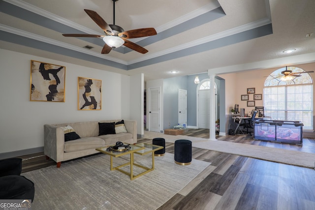 living area featuring a healthy amount of sunlight, wood finished floors, a ceiling fan, and a tray ceiling