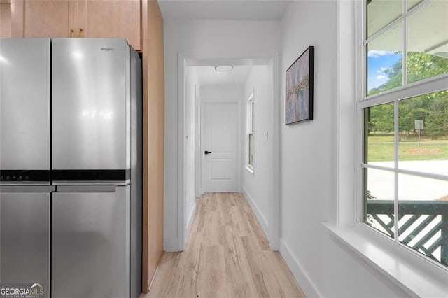 hall featuring baseboards, a healthy amount of sunlight, and light wood-style floors