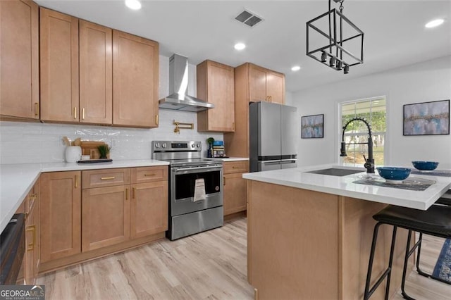 kitchen with stainless steel appliances, a sink, tasteful backsplash, light wood-type flooring, and wall chimney range hood