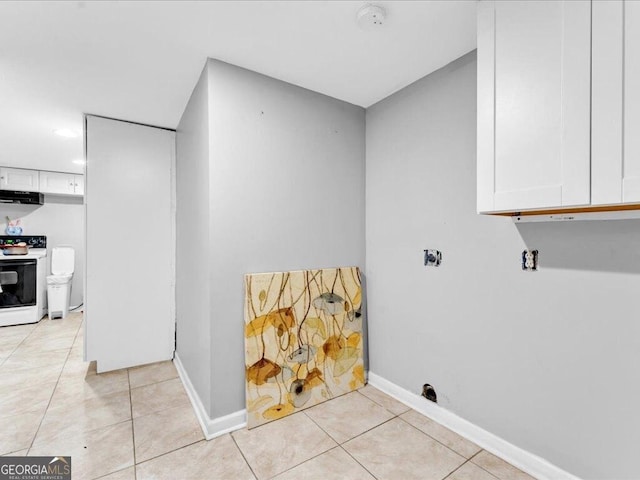 clothes washing area featuring light tile patterned flooring, cabinet space, and baseboards