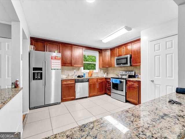 kitchen with light tile patterned floors, backsplash, appliances with stainless steel finishes, and light stone counters