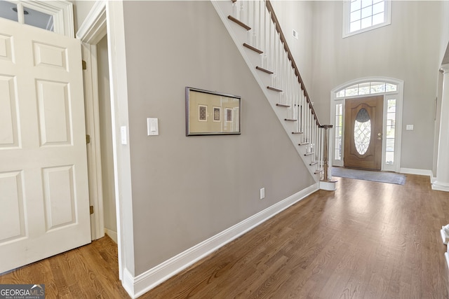 foyer featuring baseboards, wood finished floors, a towering ceiling, and stairs
