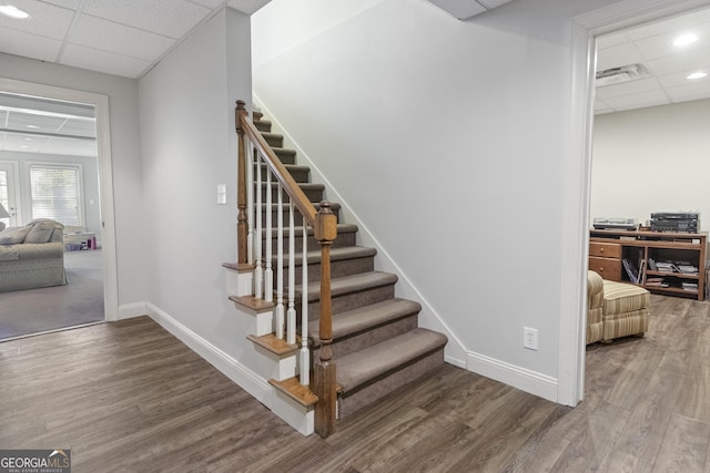staircase with baseboards, wood finished floors, and a drop ceiling