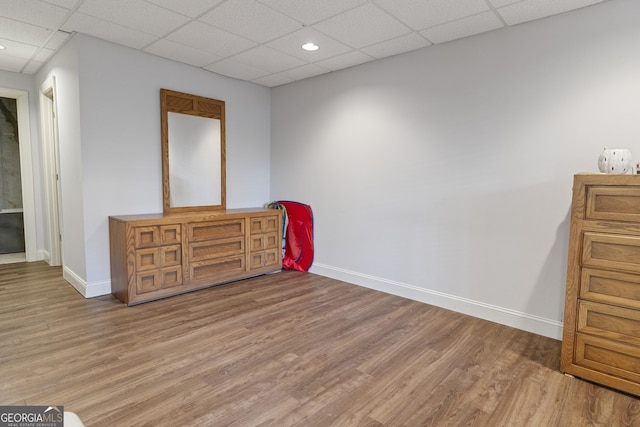 interior space featuring a paneled ceiling, baseboards, and light wood-style floors