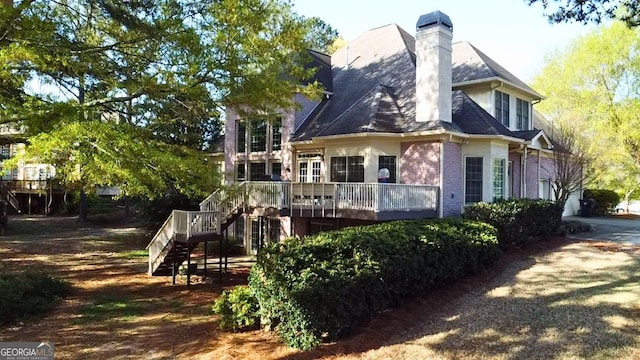 back of house featuring a chimney, brick siding, a deck, and stairs