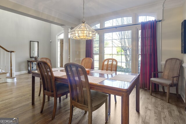 dining space featuring ornate columns, crown molding, a chandelier, light wood-style flooring, and stairs