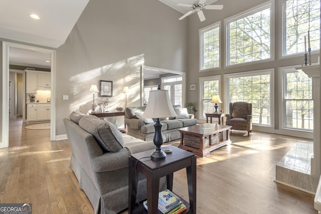 living room with ceiling fan, a towering ceiling, light wood-type flooring, and plenty of natural light