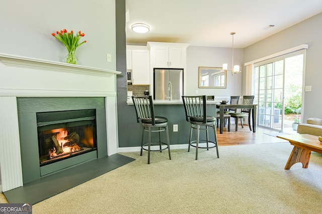 kitchen with white cabinets, light carpet, a chandelier, a kitchen bar, and stainless steel refrigerator