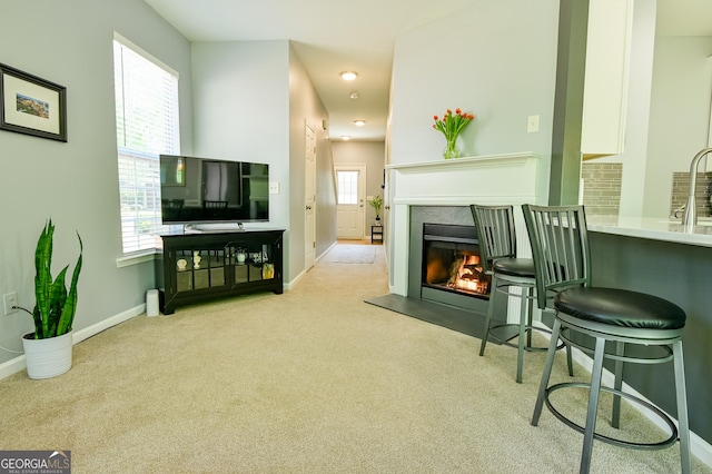 carpeted living area with baseboards, a glass covered fireplace, a sink, and recessed lighting