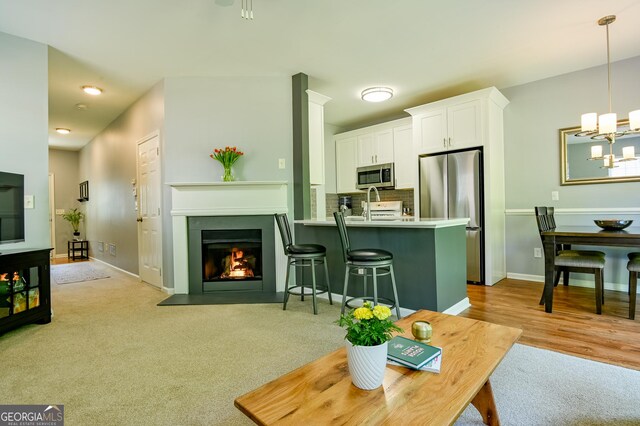 living area with a fireplace with flush hearth, baseboards, a notable chandelier, and light colored carpet