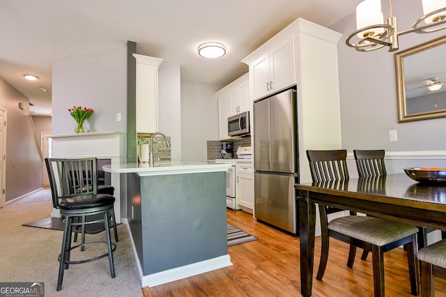 kitchen with a breakfast bar, stainless steel appliances, light countertops, white cabinets, and a notable chandelier