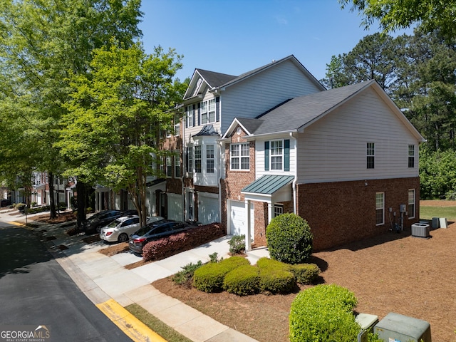 view of front of house featuring central AC unit, brick siding, roof with shingles, and a garage
