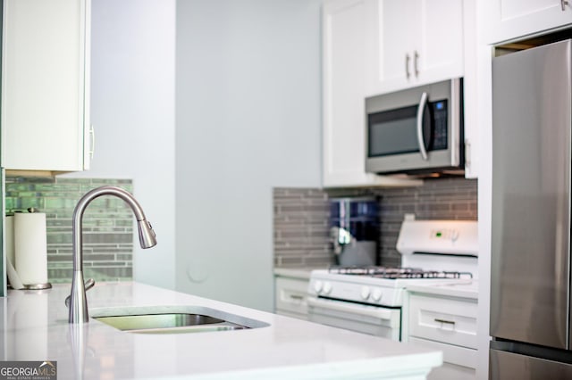 kitchen featuring white cabinets, backsplash, light countertops, a sink, and appliances with stainless steel finishes