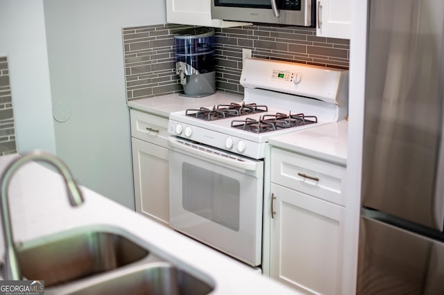 kitchen with white cabinets, white range with gas stovetop, a sink, freestanding refrigerator, and tasteful backsplash