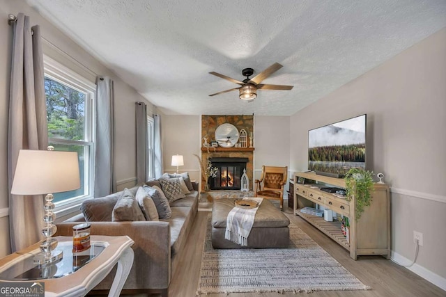 living area with a textured ceiling, baseboards, a ceiling fan, wood finished floors, and a fireplace