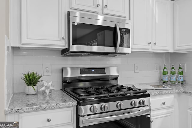 kitchen with white cabinets, stainless steel appliances, light stone counters, and decorative backsplash
