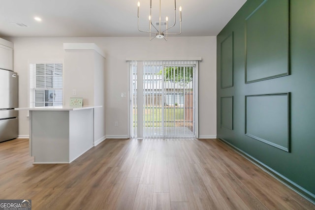 unfurnished dining area with a chandelier, visible vents, wood finished floors, and baseboards