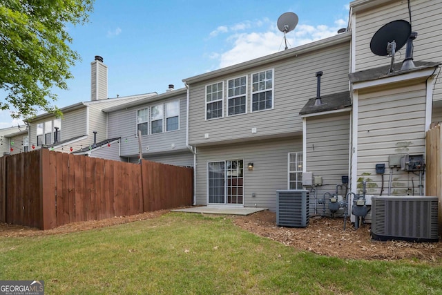 back of property featuring a lawn, central air condition unit, a chimney, and fence
