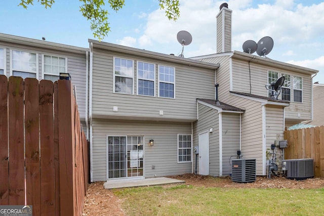 rear view of property with a lawn, central air condition unit, a chimney, and fence