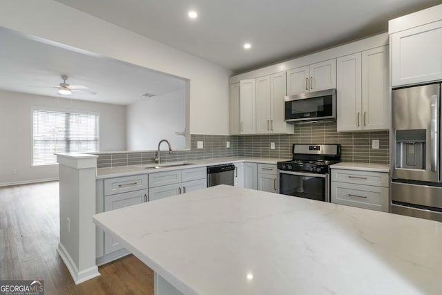 kitchen with ceiling fan, a sink, a peninsula, backsplash, and appliances with stainless steel finishes