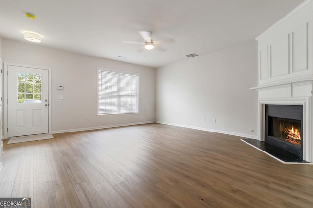 unfurnished living room featuring wood finished floors, a ceiling fan, a fireplace, visible vents, and baseboards