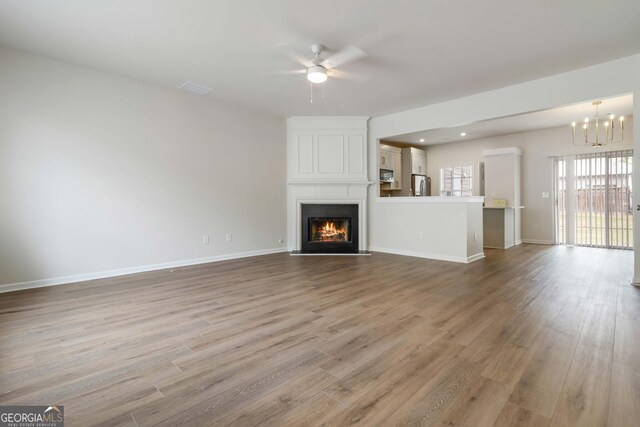 unfurnished living room with baseboards, wood finished floors, ceiling fan with notable chandelier, and a fireplace