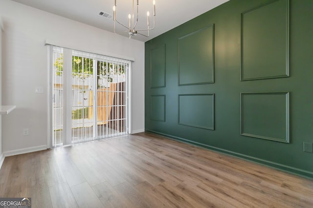 empty room with a notable chandelier, baseboards, visible vents, and wood finished floors