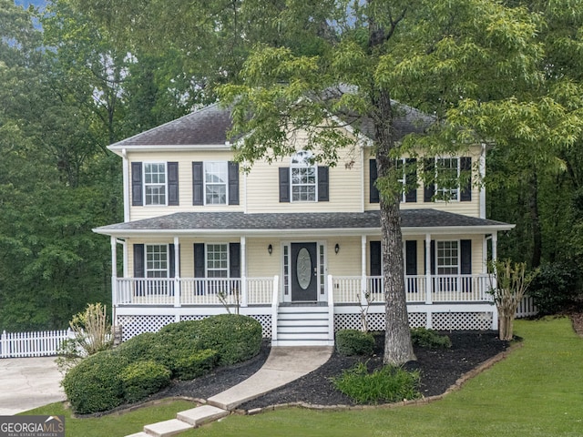 colonial home with covered porch, fence, a front lawn, and roof with shingles