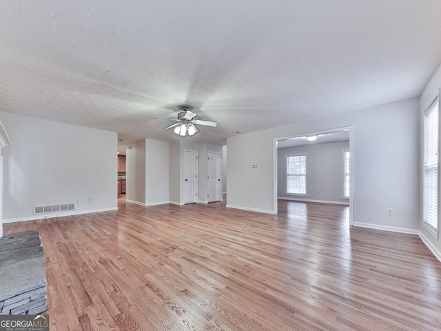 unfurnished living room with ceiling fan, light wood finished floors, baseboards, visible vents, and a textured ceiling