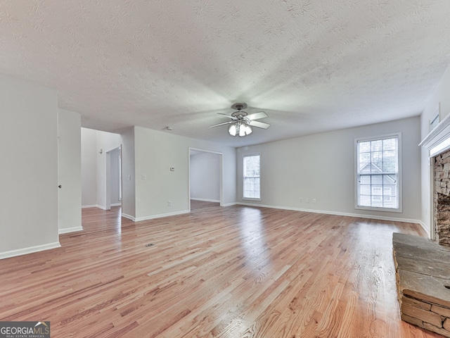 unfurnished living room with light wood finished floors, ceiling fan, a stone fireplace, and plenty of natural light