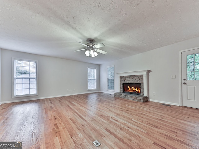 unfurnished living room with light wood finished floors, a fireplace, ceiling fan, visible vents, and a textured ceiling