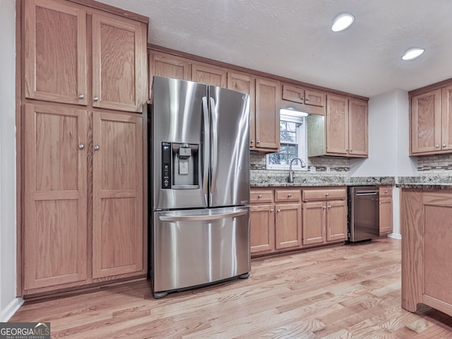 kitchen featuring appliances with stainless steel finishes, stone counters, light wood-type flooring, and a sink