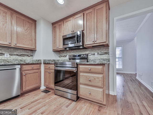 kitchen featuring stainless steel appliances, decorative backsplash, light wood-type flooring, crown molding, and light stone counters