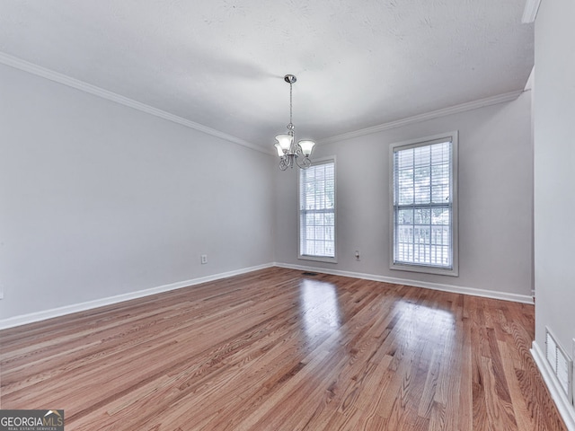 spare room featuring an inviting chandelier, ornamental molding, light wood-type flooring, baseboards, and visible vents