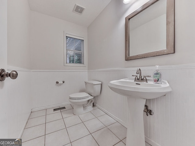 bathroom featuring toilet, tile patterned flooring, visible vents, and wainscoting