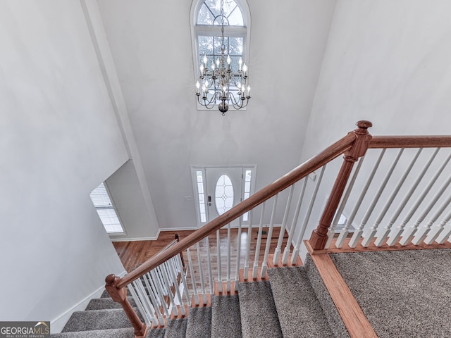 stairway featuring a towering ceiling, a notable chandelier, wood finished floors, and baseboards