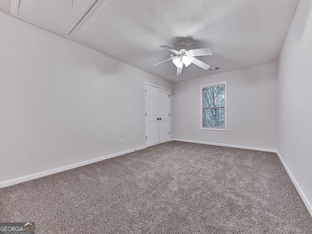 carpeted spare room with attic access, visible vents, ceiling fan, and baseboards