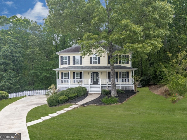 colonial-style house with a porch, a front yard, a shingled roof, concrete driveway, and fence