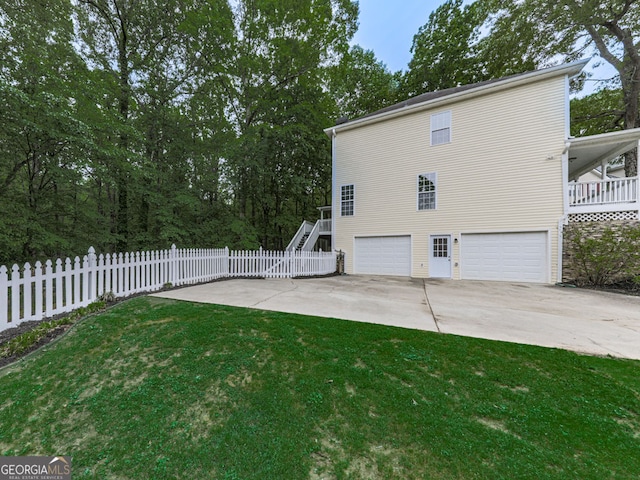 view of side of property featuring a lawn, stairs, concrete driveway, an attached garage, and fence