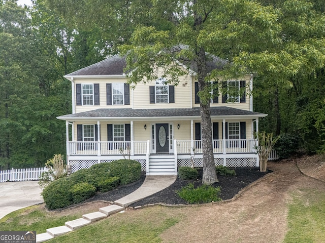 colonial house featuring a porch, roof with shingles, and fence