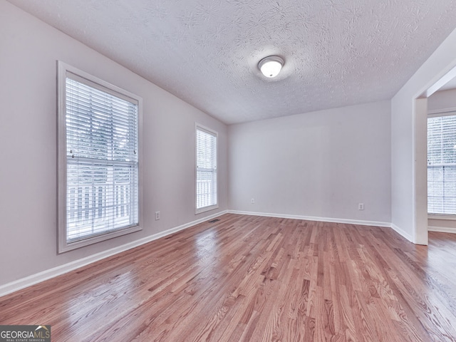 unfurnished room with a textured ceiling, visible vents, light wood-style flooring, and baseboards